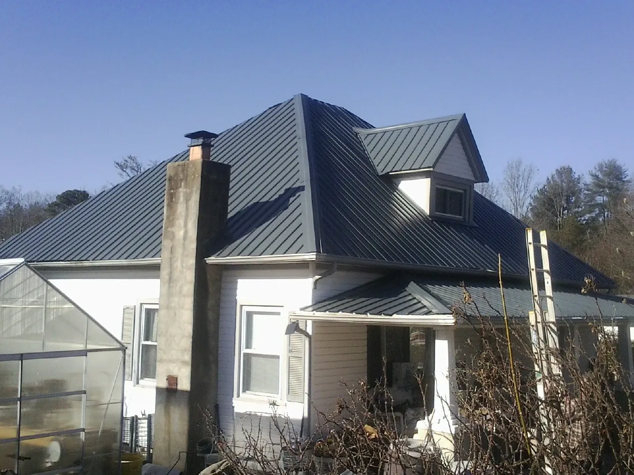 Dark blue standing seam metal roof on a white farmhouse with dormer — Slate & Tile Roof Repair by Roofing Brothers in Whiteman Air Force Base