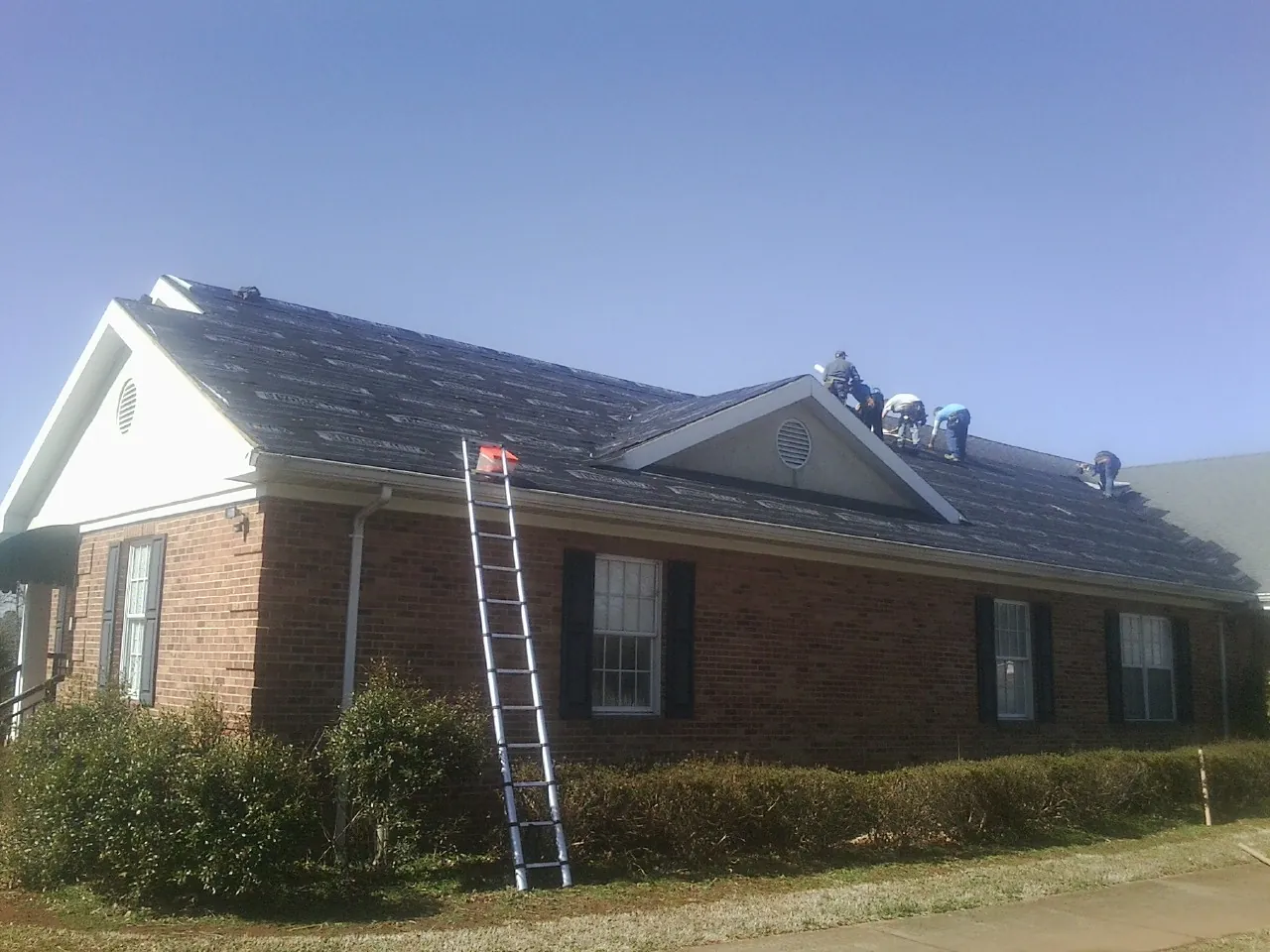 Crew tearing shingles off a brick ranch roof with a ladder set — Emergency Roof Repair work by our crew in Whiteman Air Force Base