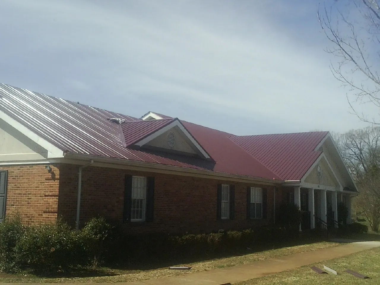 Red metal roof with gabled entries on a long brick building, from a Hail Damage Roof Repair job in Whiteman Air Force Base