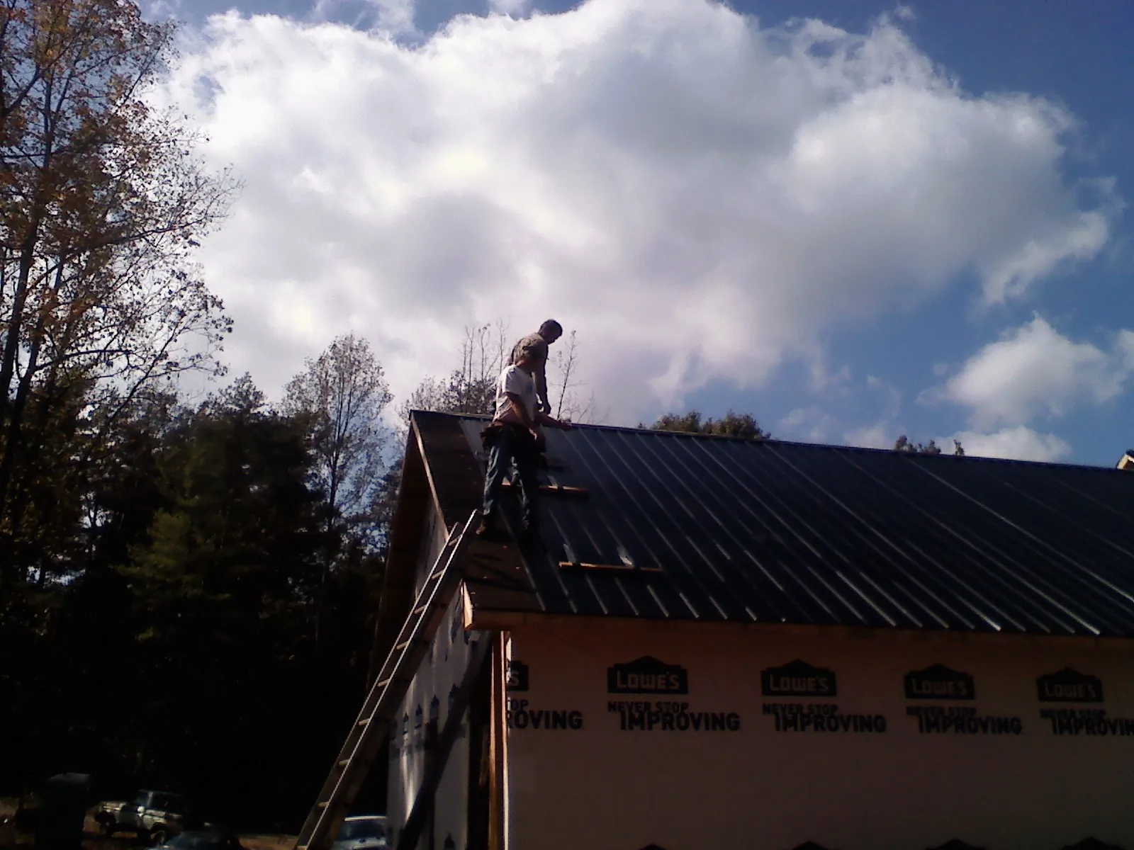 Roofer fastening dark metal panels high against a cloudy sky, from a Roof Inspection job in Whiteman Air Force Base