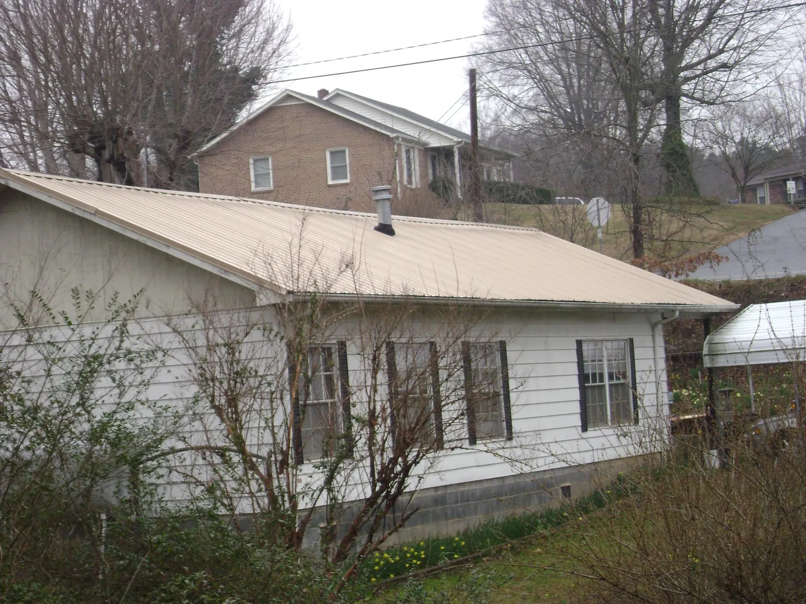Tan metal roof on a white sided house set into a hillside — Commercial Roofing by Roofing Brothers in Whiteman Air Force Base
