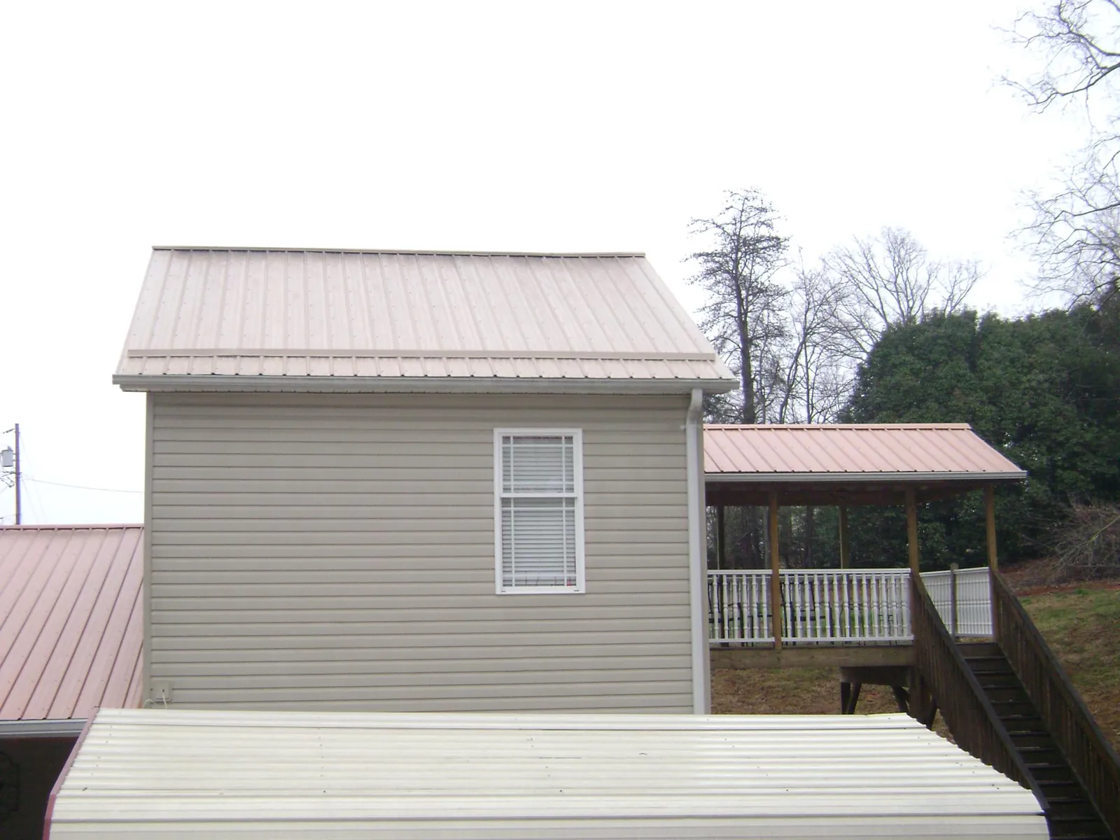 Tan metal roofs on a two story addition and attached porch, from a Roof Replacement job in Whiteman Air Force Base